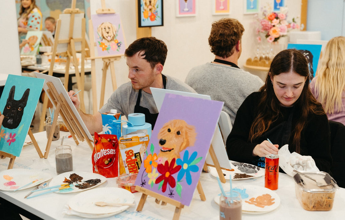 Couples painting colorful pet portraits at a paint and sip studio, enjoying snacks, drinks, and a fun, creative date night in a relaxed setting