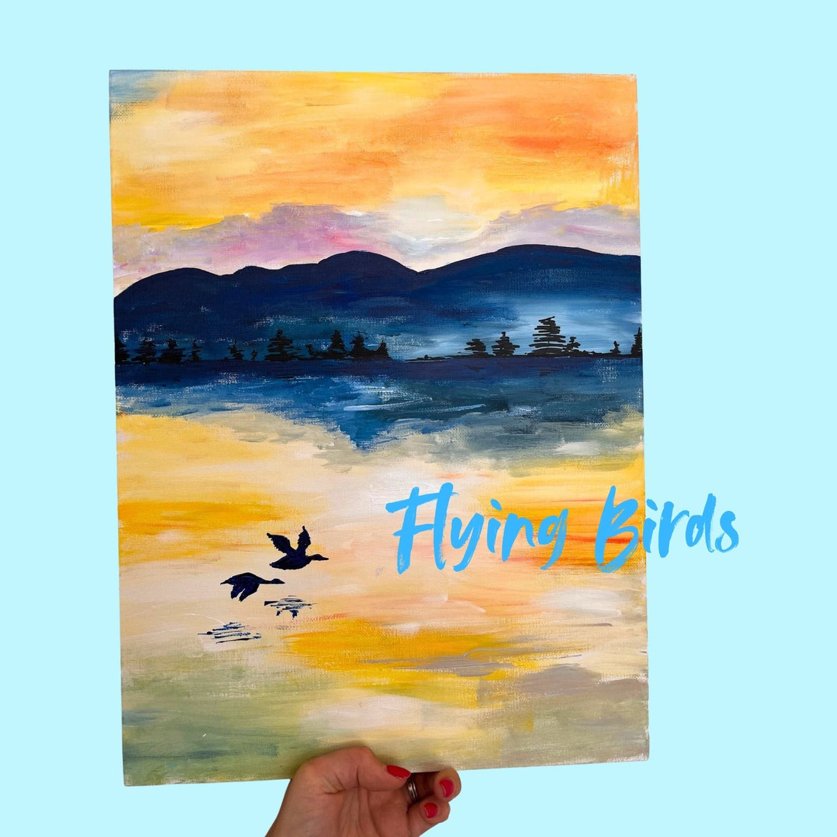 A hand holds a vertical canvas painting depicting a sunset landscape with mountains, water, and flying birds. The painting features a vibrant orange and yellow sky, blue mountains, and reflective water.