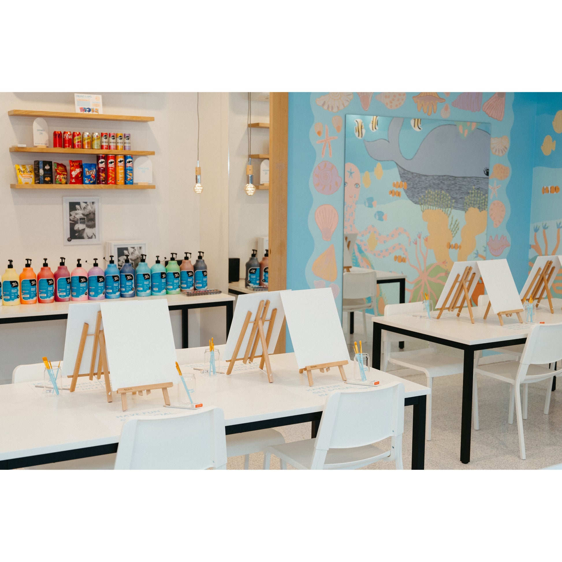 Art studio with tables, chairs, and art supplies against a colorful wall.